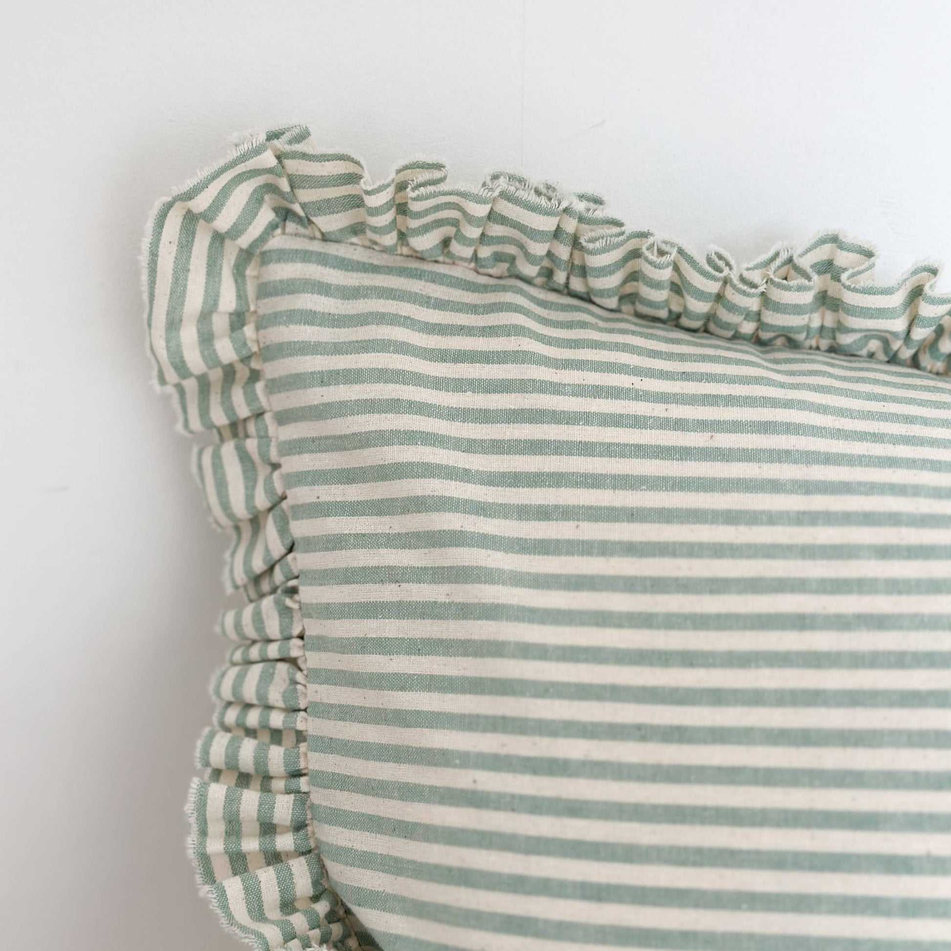 Green and white striped pillow with ruffled edges on a light background