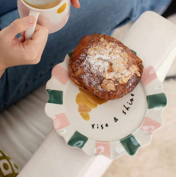 Person holding a cup of coffee with a pastry on a decorative plate.
