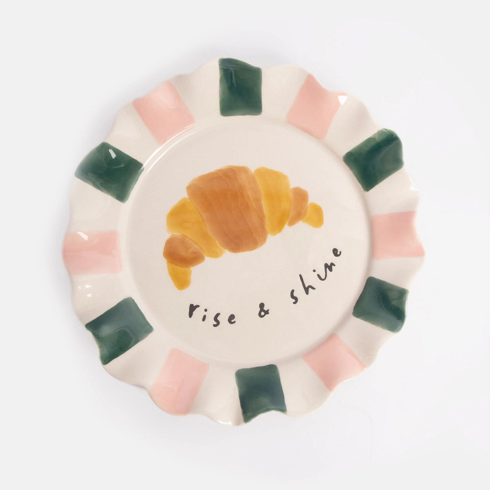 Decorative plate with a croissant illustration and 'Rise & Shine' text on a white background
