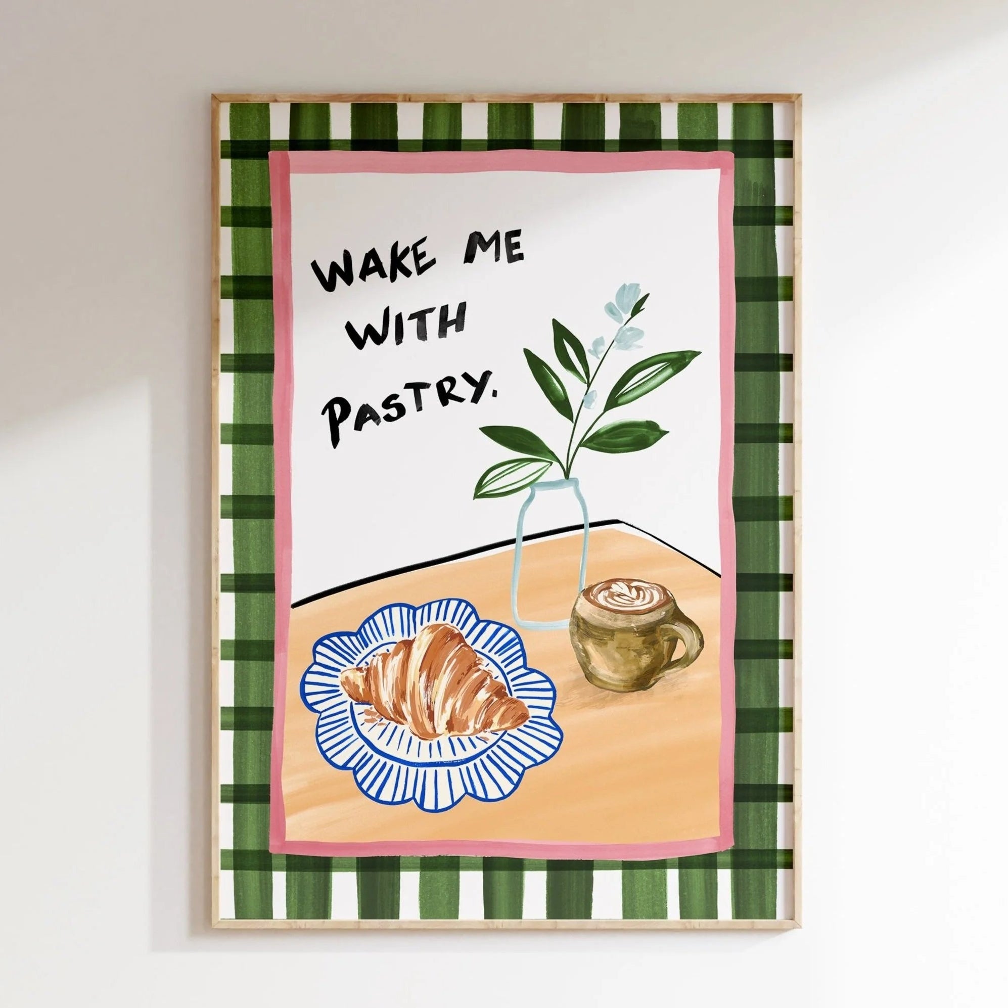 Framed artwork with a plaid border, 'Wake Me with Pastry' text, and illustrations of a croissant and coffee.