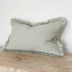 Striped pillow with ruffled edges on a wooden surface against a white wall