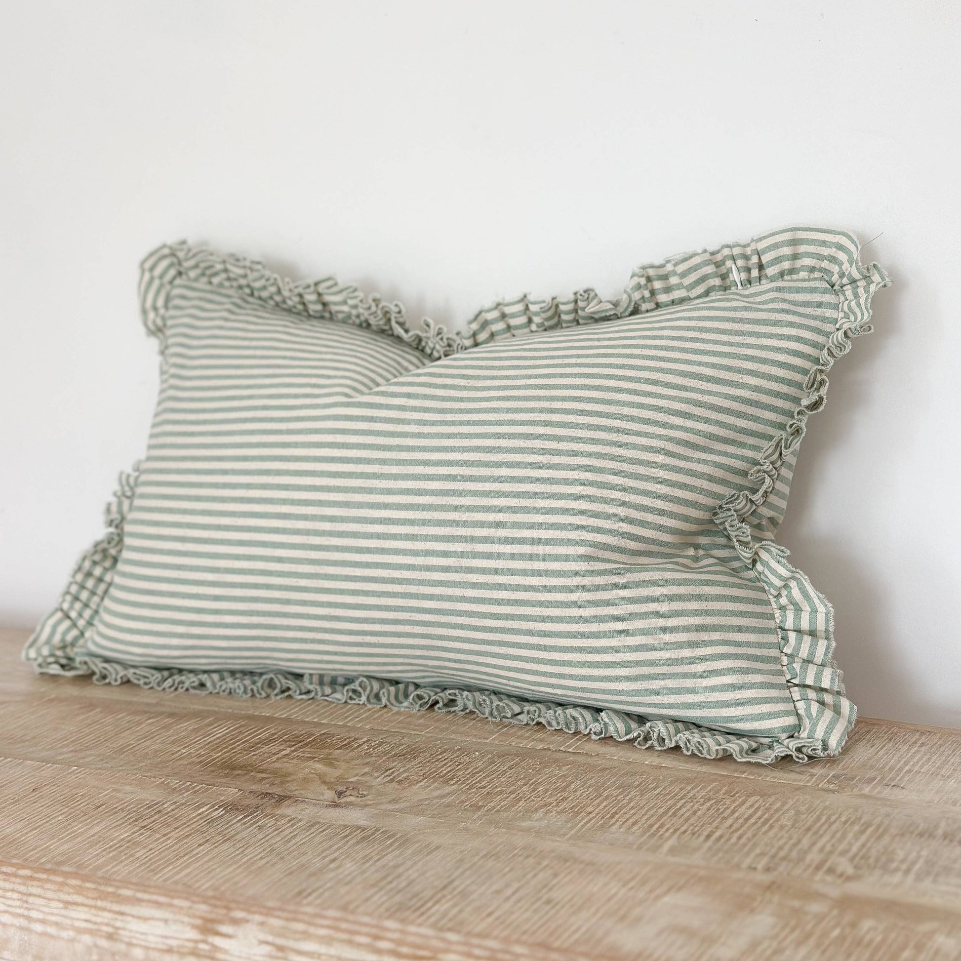 Striped pillow with ruffled edges on a wooden surface against a white wall