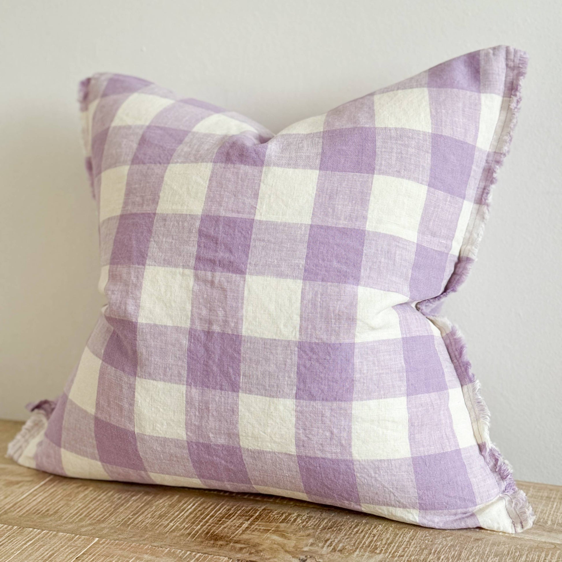 Purple and white checkered pillow on a wooden surface with a neutral background