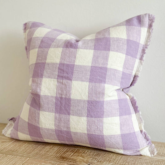 Purple and white checkered pillow on a wooden surface with a neutral background