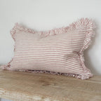 Pink striped pillow with ruffles on a wooden surface against a white wall