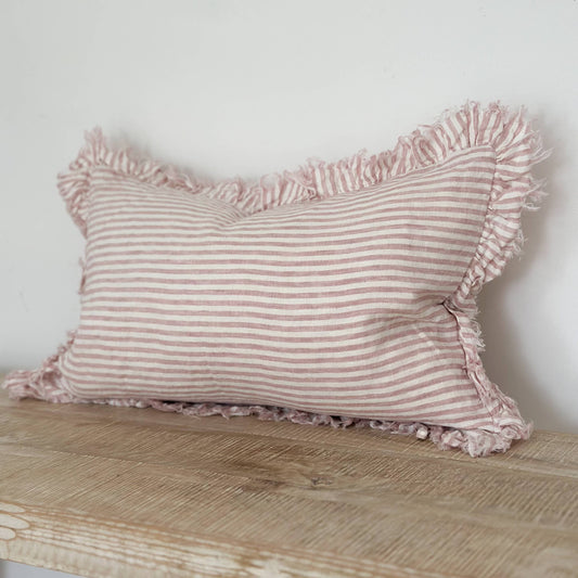 Pink striped pillow with ruffles on a wooden surface against a white wall