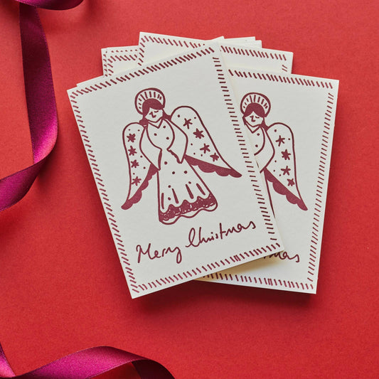 Stack of Christmas cards with angel design on a red background with pink ribbons.