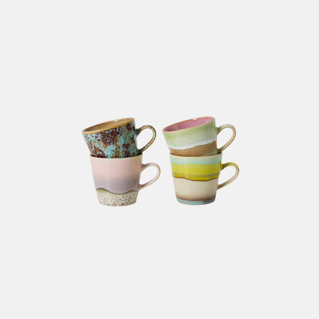 Two stacked ceramic mugs with pastel and earthy multicolor designs, including pink, yellow, green, and brown tones, set against a plain light gray background.