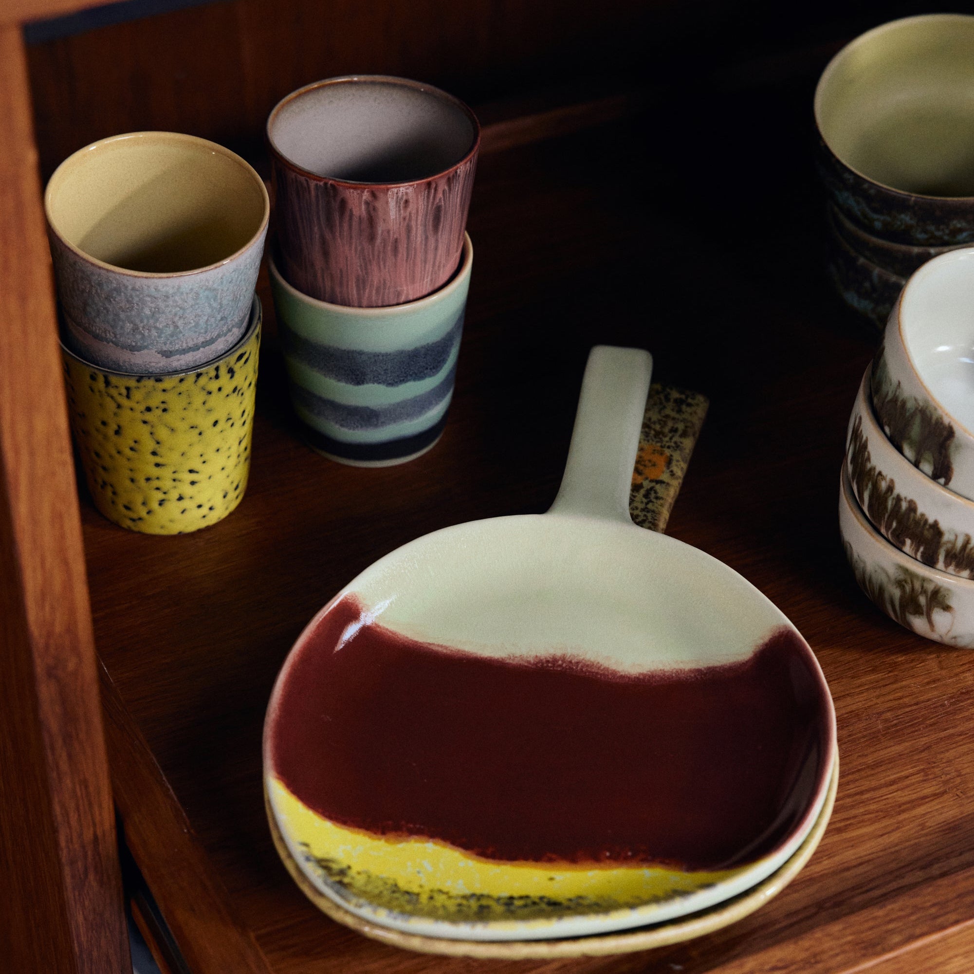 Stacked ceramic dishes and cups on a wooden shelf