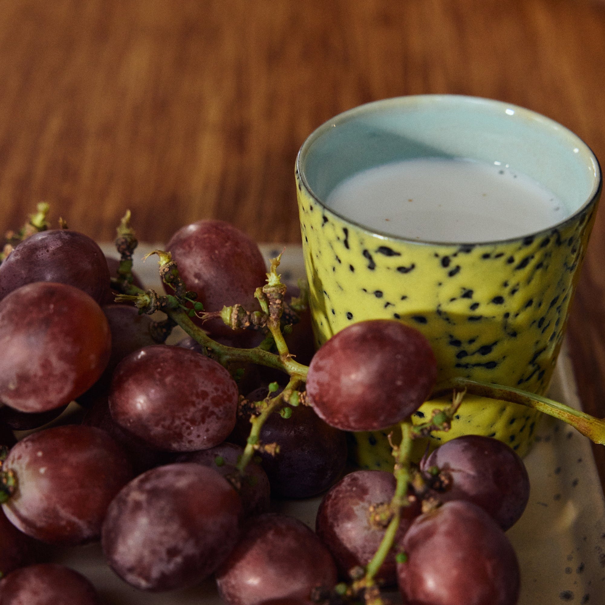 Bunch of grapes on a plate with a yellow and black spotted cup in the background.