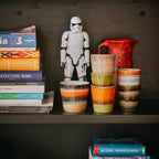 Shelf with books, a Stormtrooper figurine, and colorful ceramic cups.