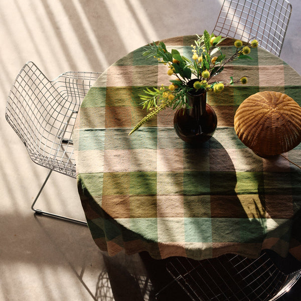 Round table with a checkered tablecloth, vase of flowers, and decorative ball under a white curtain.