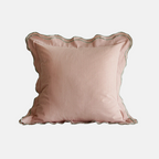 A square blush pink pillow with a scalloped edge and subtle vertical ribbed texture, shown against a plain light gray background.