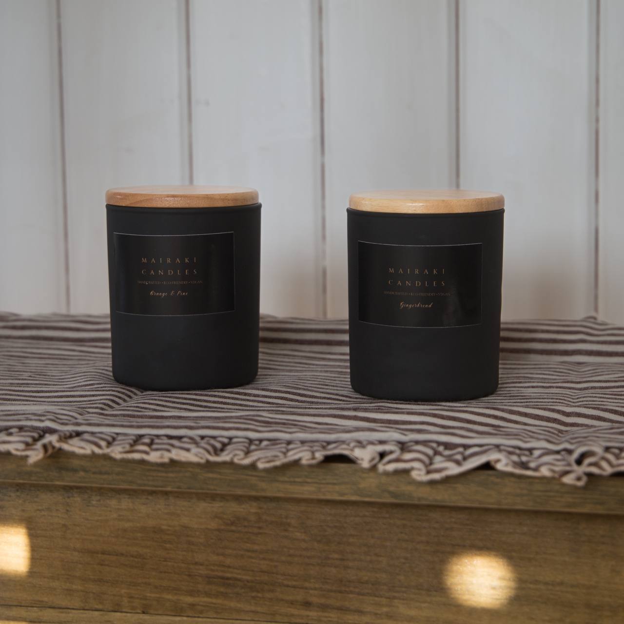 Two black candles with wooden lids on a striped fabric surface.
