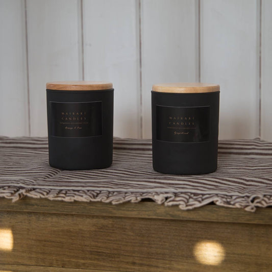 Two black candles with wooden lids on a striped fabric surface.