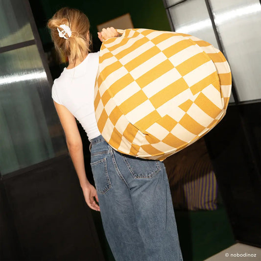 Person holding a large yellow and white checkered  bean bag apgainst a modern indoor background