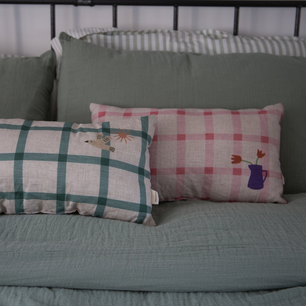 nobodinoz linen cushions in green check and pink check displayed on a bed next to each other