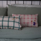 nobodinoz linen cushions in green check and pink check displayed on a bed next to each other