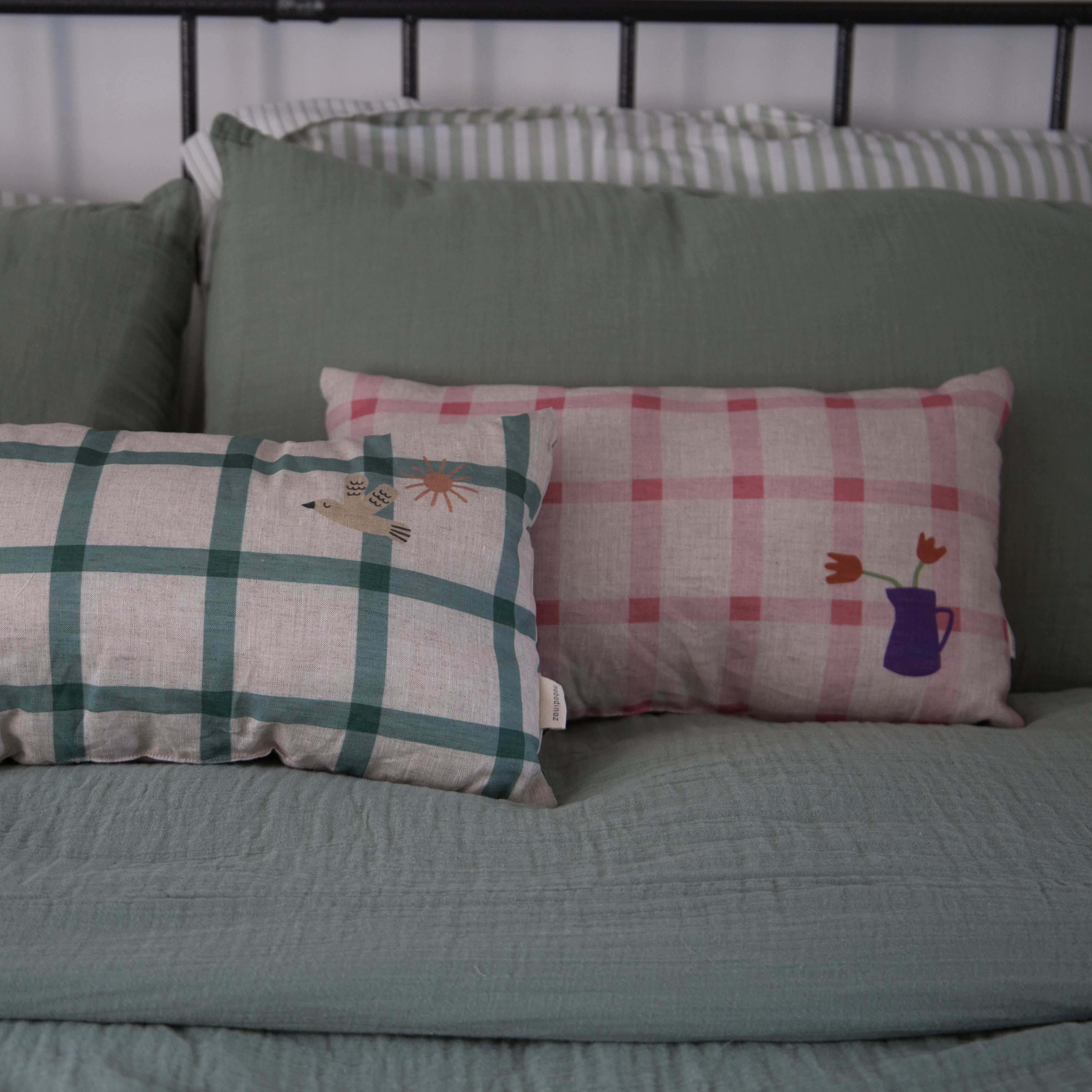 nobodinoz linen cushions in green check and pink check displayed on a bed next to each other