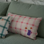 nobodinoz pink checkered cushion displayed next to the same one in green on a green linen bedsheet