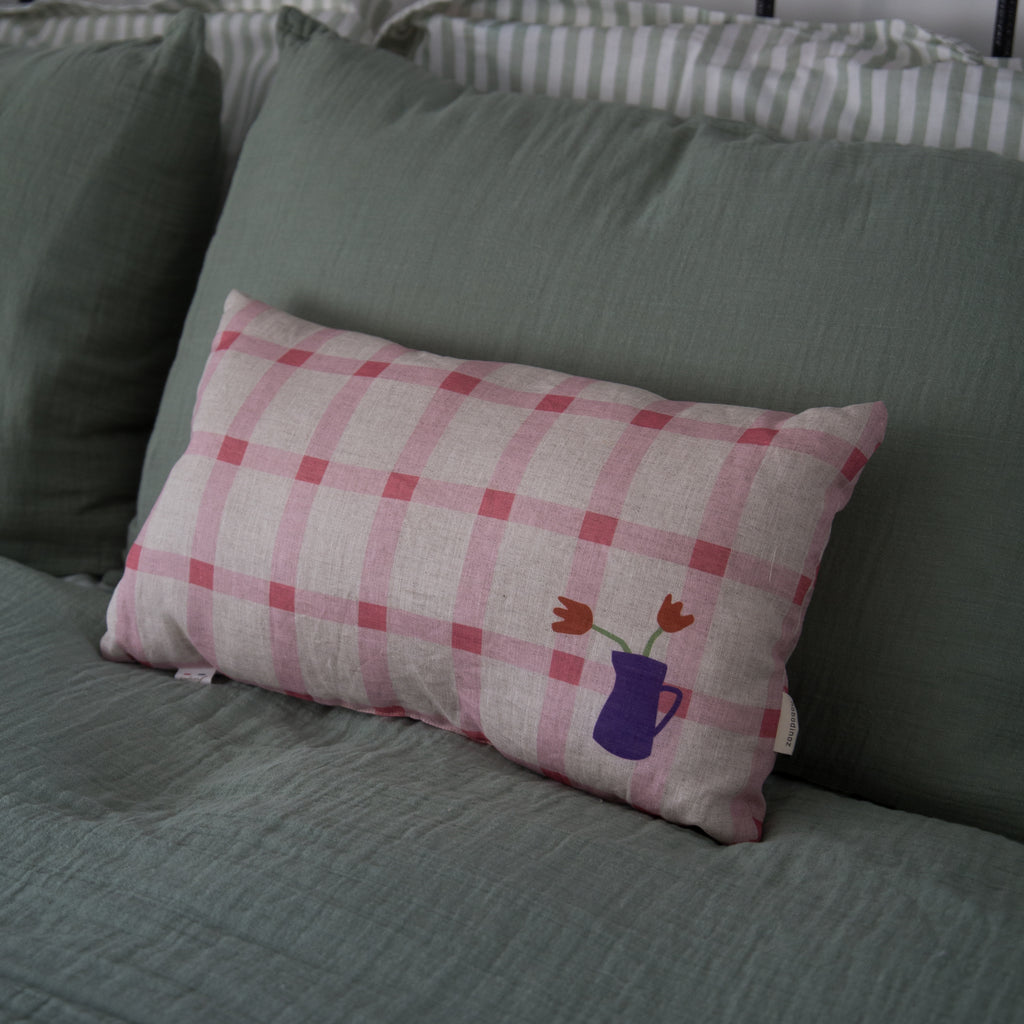 Nobodinoz pink tulip checkered throw cushion displayed on a bed with a green linen cover 
