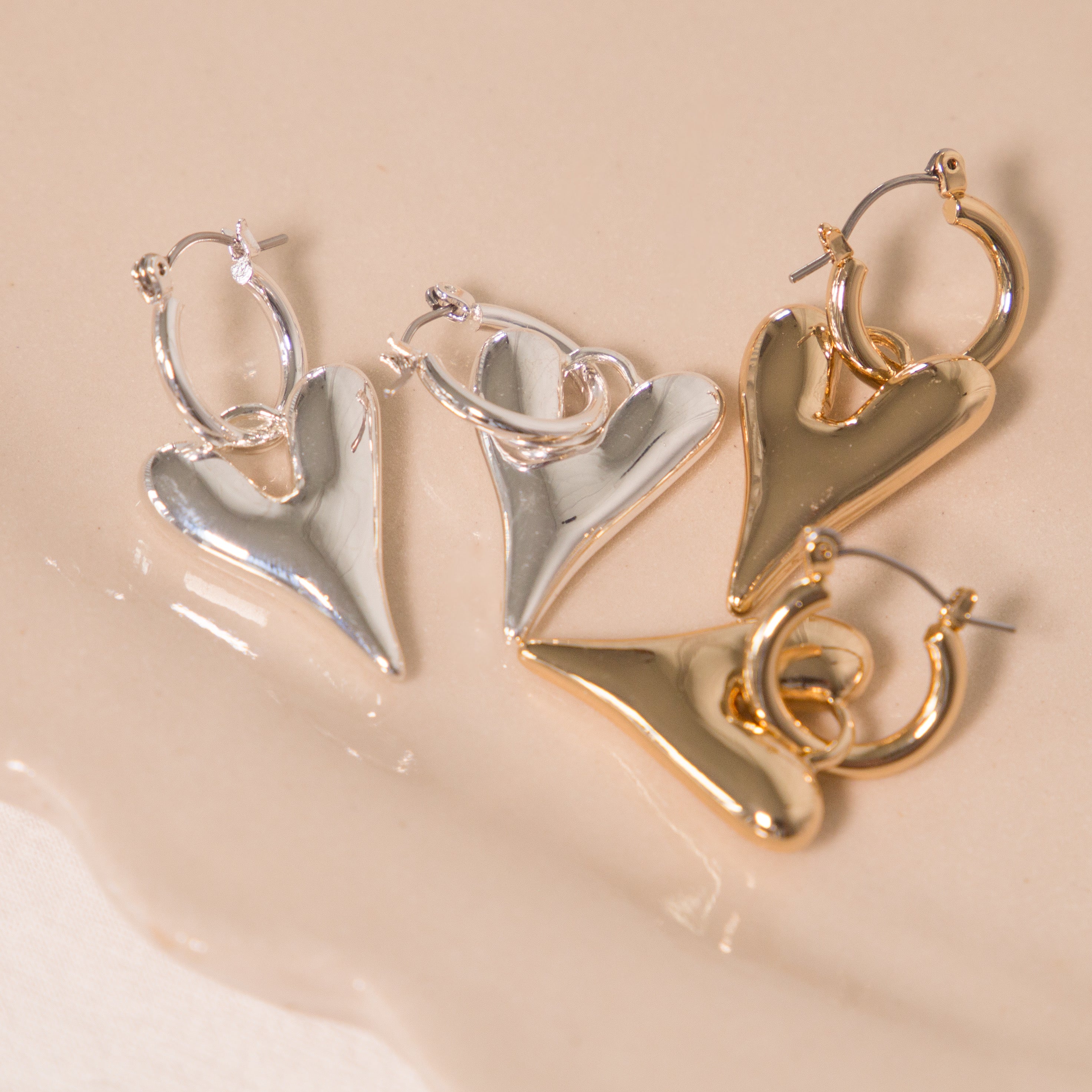 Pair of heart-shaped earrings in silver and gold on a beige surface