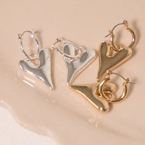 Pair of heart-shaped earrings in silver and gold on a beige surface