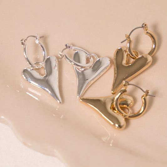 Pair of heart-shaped earrings in silver and gold on a beige surface