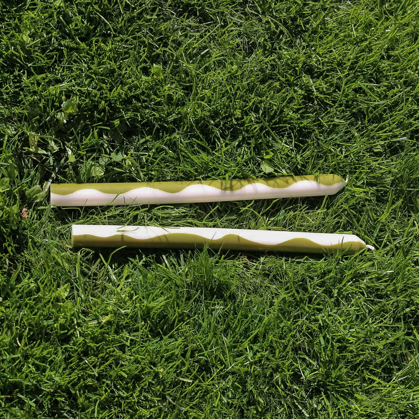 Dinner candles in green and white with a swirl pattern displaying each colour on either side. Set of two laying on the grass. 
