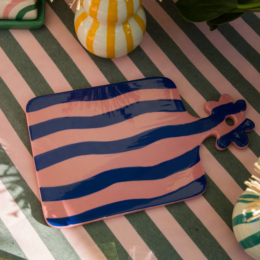 Que Rico Ceramic tray in pink and blue stripe with a flower handle glazed. Displayed on a stripe tablecloth 