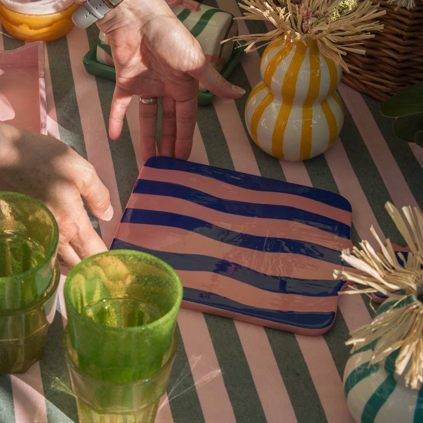 Pink and Blue wiggle striped ceramic tray displayed on an outside table scene with a model placing the tray down 