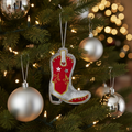 Decorative cowboy boot ornament hanging on a tree with Christmas decorations.