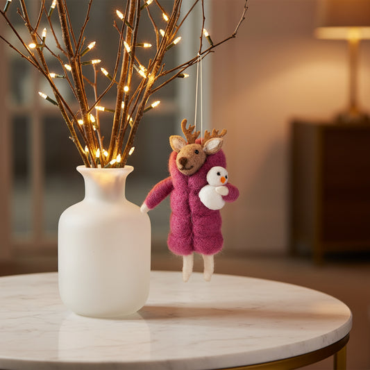 Felted reindeer ornament wearing a pink coat holding a snowman on a white background