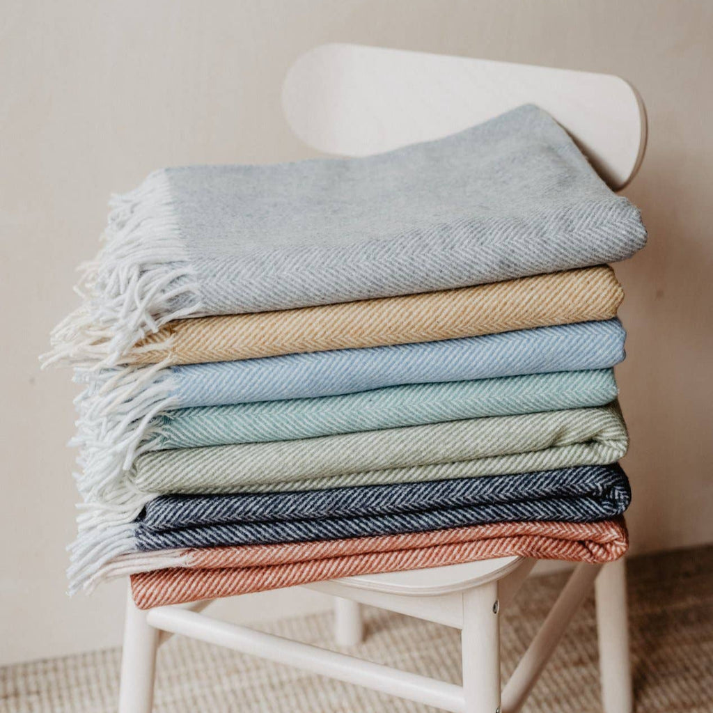 TBCo knee blankets in various colours folded and displayed on a chair.