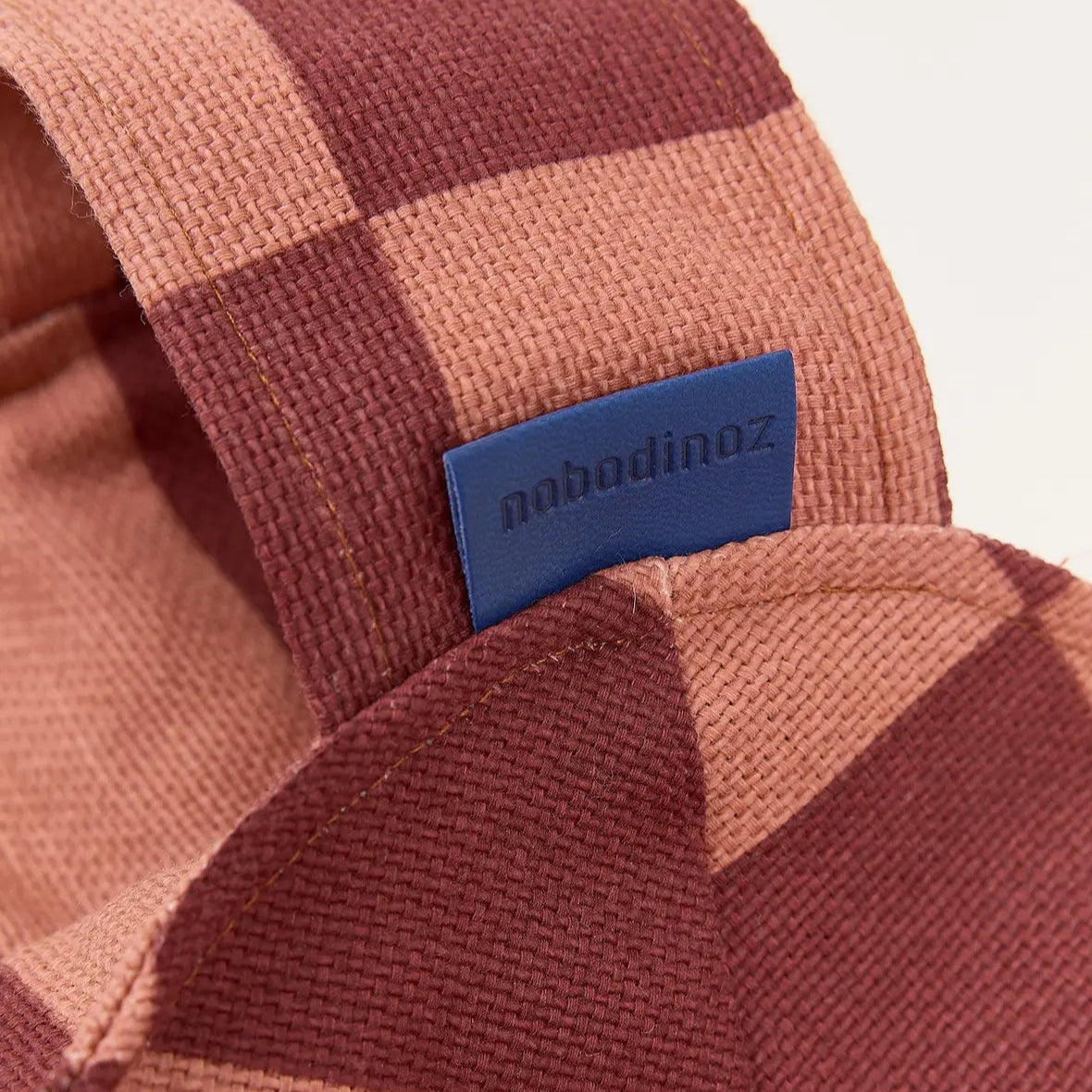 Close-up of a checkered fabric strap with a blue label on a beige background
